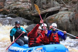 Three people in a blue raft with a guide in the back going through Horcerace rapids on the Peshtigo River