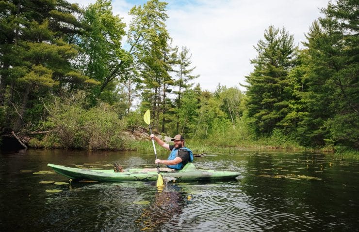 A man paddles a kayak through lily pads on high falls flowage.