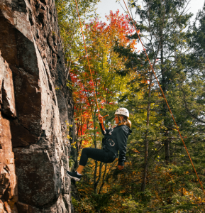 a woman rappelling down a bluff after rock climbing in Michigan